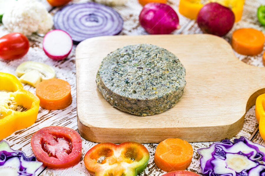 Hambúrguer vegetariano cru em tábua de corte com vegetais frescos coloridos