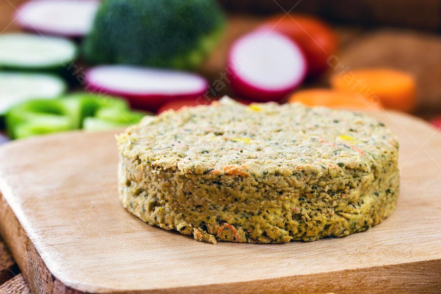 Hambúrguer vegano de vegetais em tábua de madeira com legumes coloridos