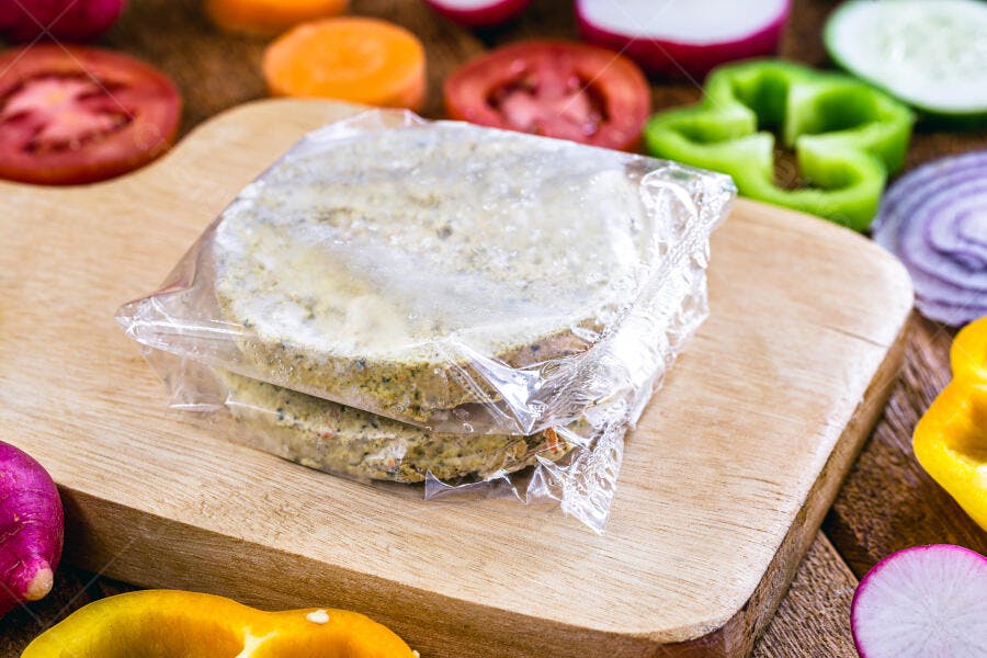 Hambúrgueres vegetais congelados em tábua com vegetais frescos coloridos
