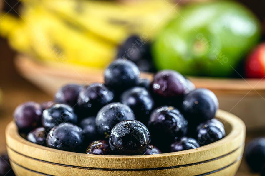 Jabuticabas frescas em tigela de madeira com frutas tropicais ao fundo