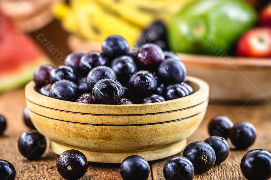 Jabuticabas frescas em tigela de madeira rústica com frutas ao fundo