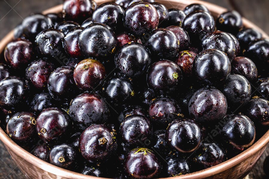 Jabuticabas frescas e roxas com gotas de água em tigela de madeira