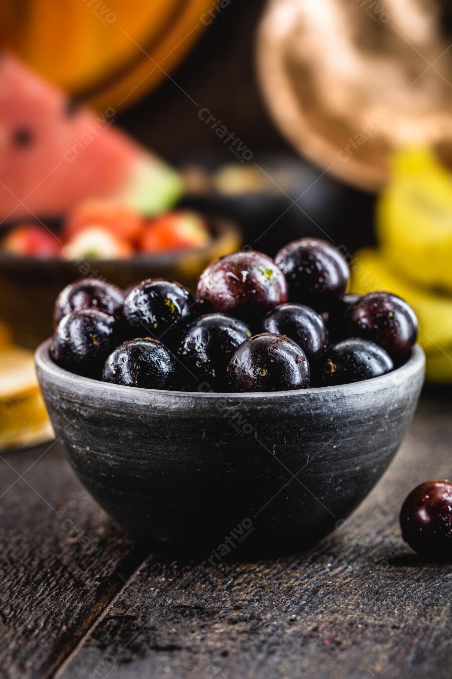 Jabuticabas frescas em tigela rústica de barro com frutas coloridas no fundo