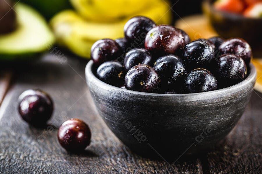 Jabuticabas frescas em tigela rústica com fundo de frutas tropicais