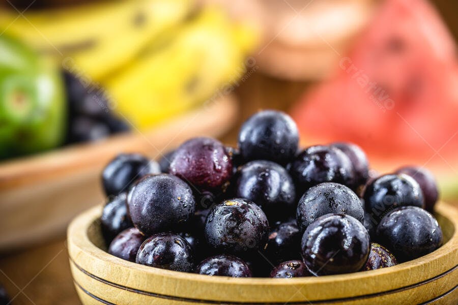 Jabuticabas frescas em tigela de madeira com frutas tropicais no fundo