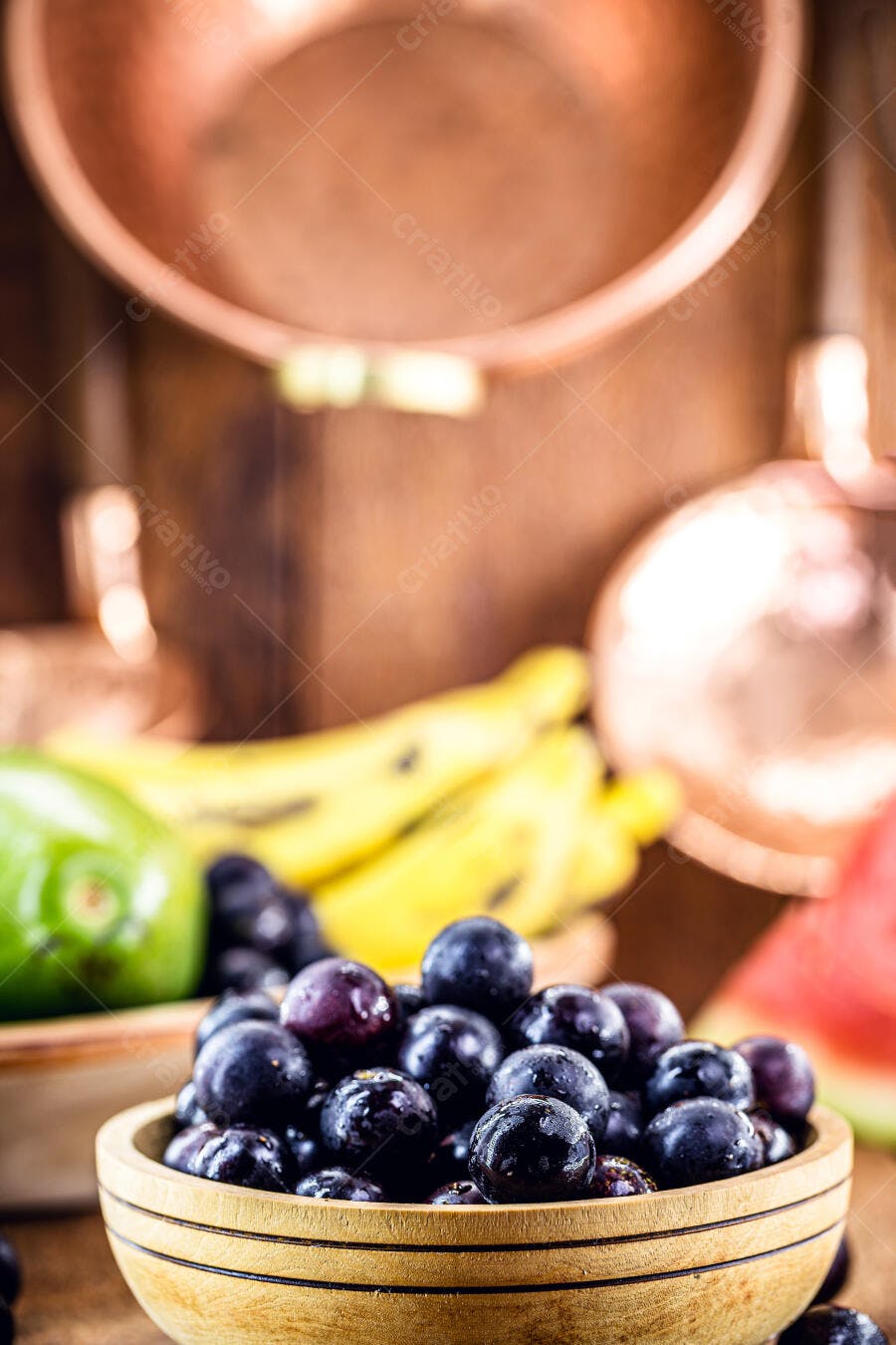 Jabuticabas frescas roxas em tigela de madeira com frutas coloridas e utensílios de cobre