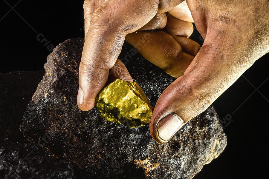 Mão de minerador segurando pepita de ouro brilhante sobre rocha escura