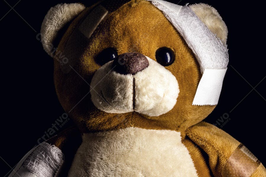 Urso de pelúcia marrom e bege ferido com ataduras em fundo escuro