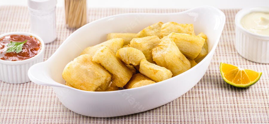 Mandioca frita dourada servida com molhos e limão em mesa clara