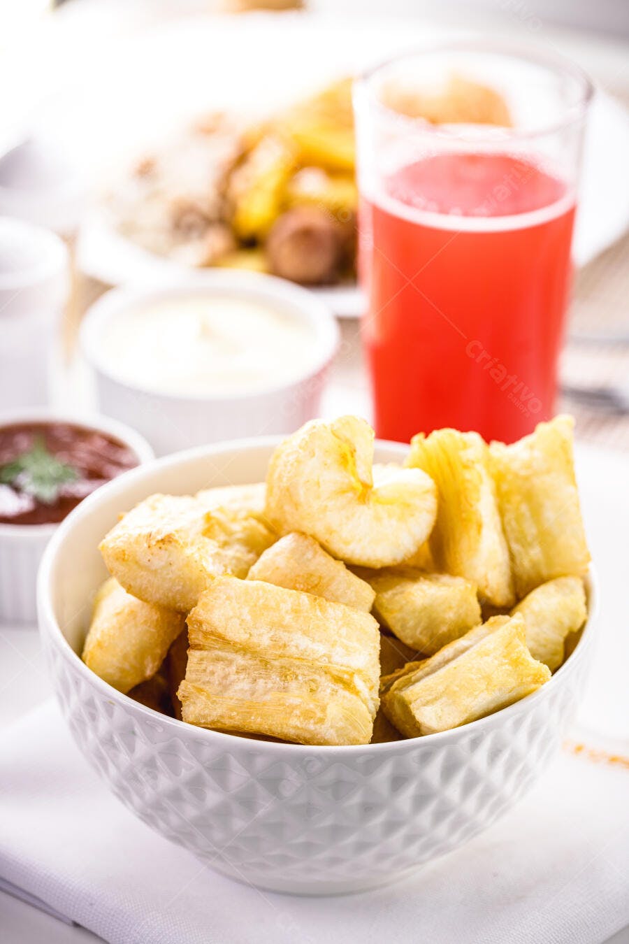 Mandioca frita crocante em tigela branca com suco e molhos em restaurante