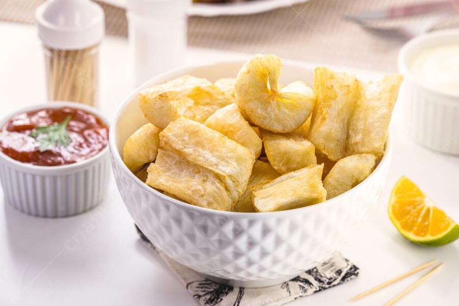 Mandioca frita dourada em tigela branca com molhos e limão