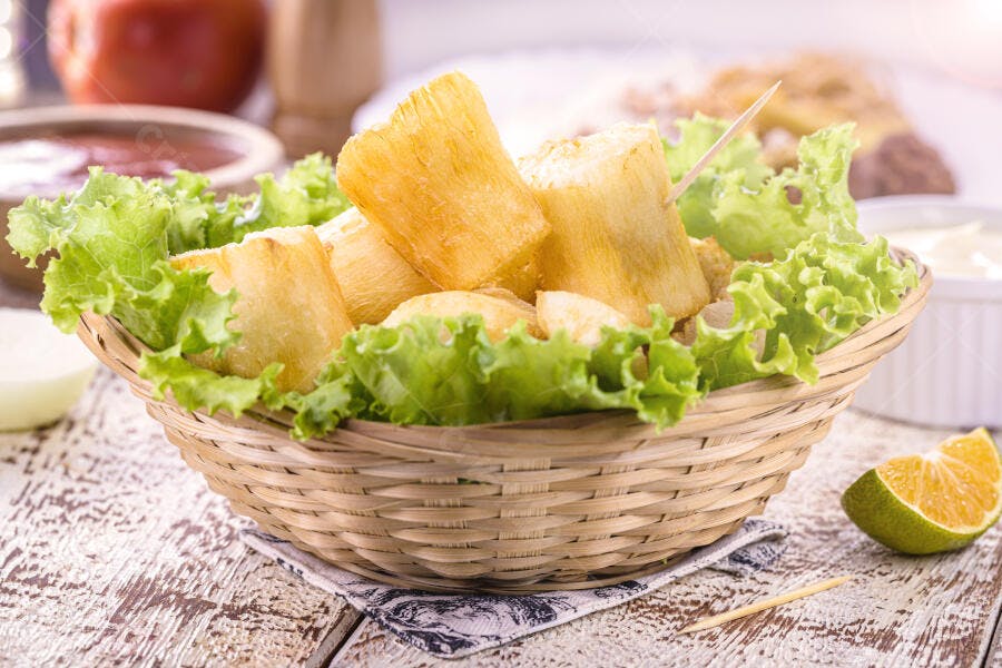 Mandioca frita crocante em cesta de vime com alface fresca e limão na mesa rústica