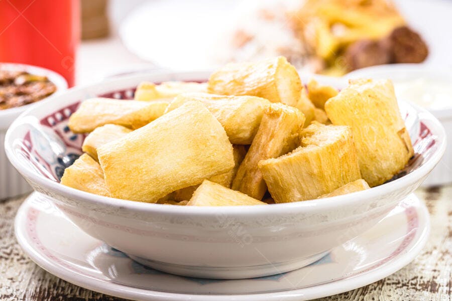 Mandioca frita dourada e crocante em tigela branca sobre mesa de madeira rústica