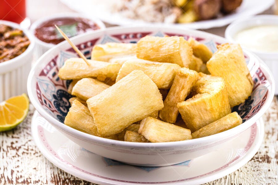 Mandioca frita dourada em tigela decorada com molhos e limão