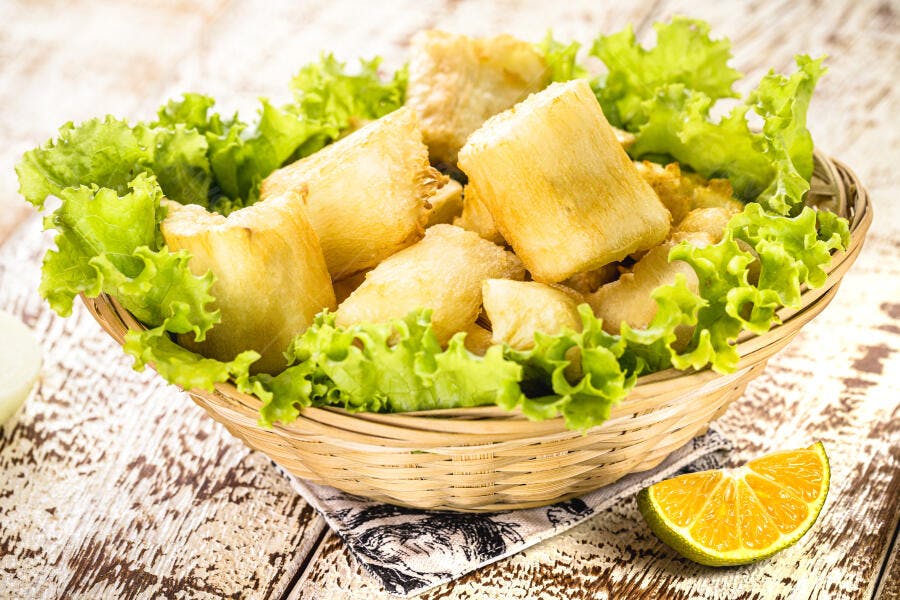 Mandioca frita dourada em cesta de vime com alface e tangerina em mesa rústica