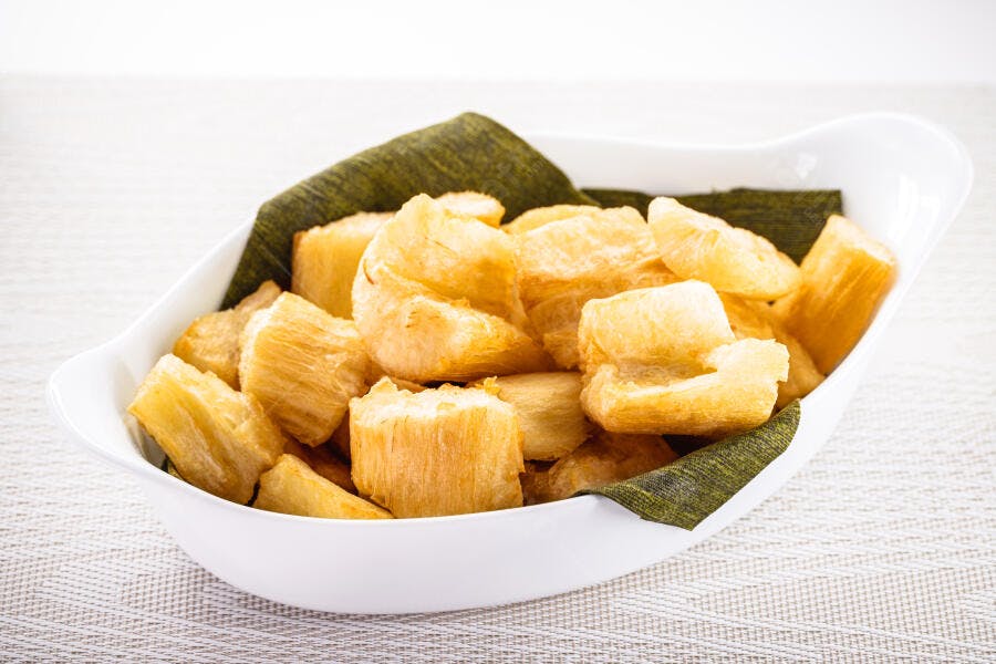 Mandioca frita dourada em tigela branca com folha verde snack brasileiro