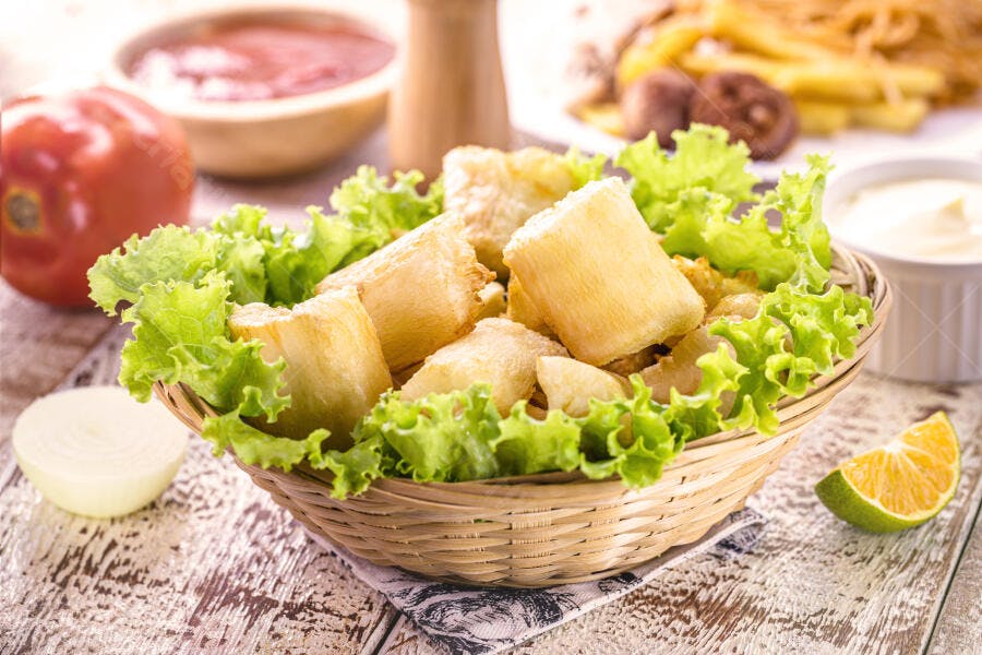 Mandioca frita dourada e crocante em cesta de vime com alface fresca e limão na mesa rústica