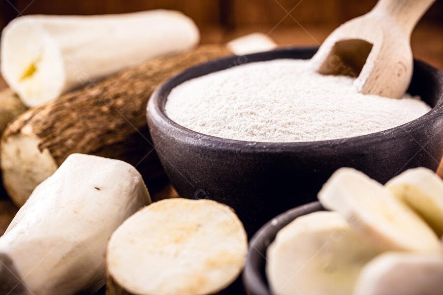 Mandioca crua e farinha branca em tigelas de barro com colher de pau