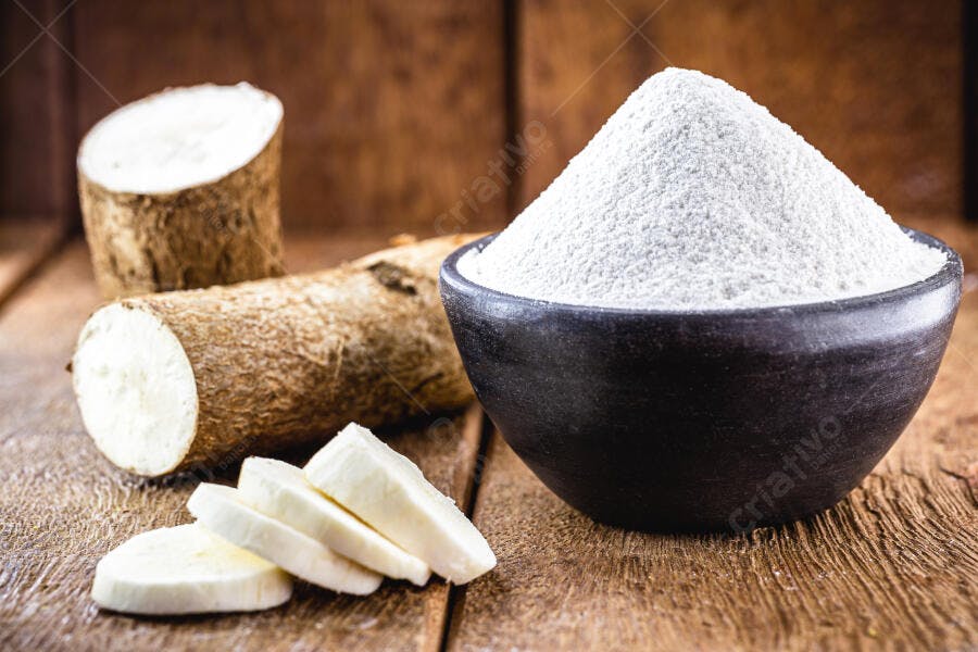 Mandioca crua fatiada e farinha de tapioca branca em tigela rústica sobre madeira escura