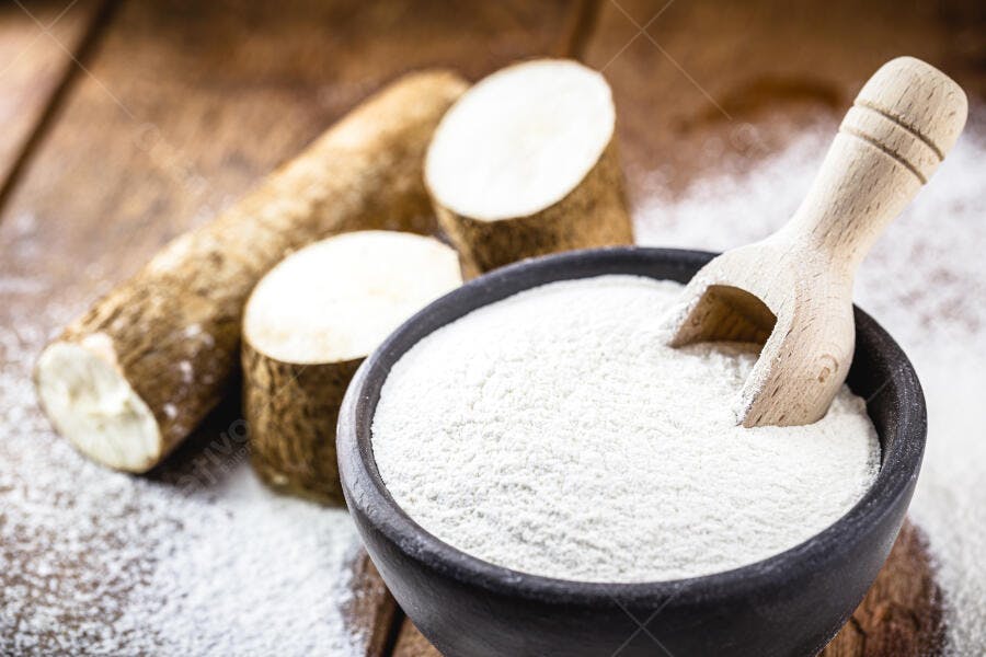 Farinha de tapioca branca em tigela rústica com mandioca crua e colher de pau