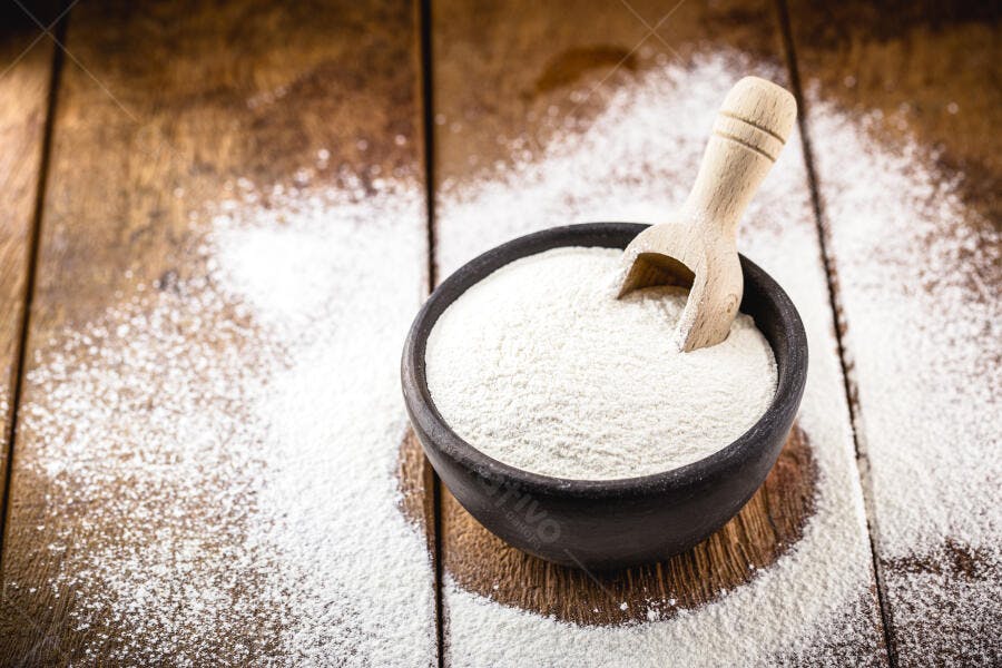 Farinha branca em tigela escura com pá de madeira em mesa rústica