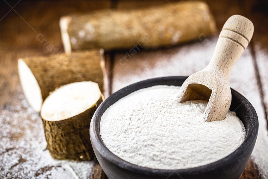 Farinha de mandioca branca e raízes de aipim descascadas em mesa rústica de madeira