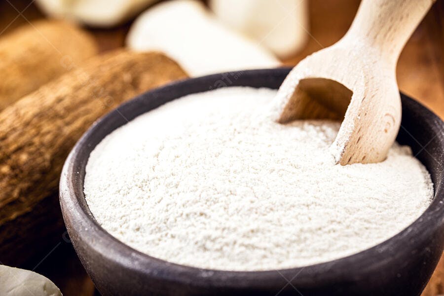 Farinha de mandioca em tigela rústica com colher de madeira e raízes