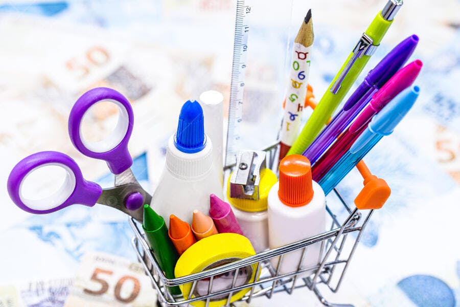 Material escolar colorido em carrinho de compras com notas de dinheiro
