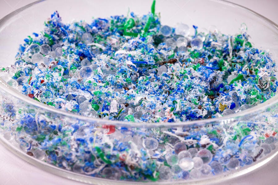 Fragmentos de microplástico azul e verde em recipiente de vidro