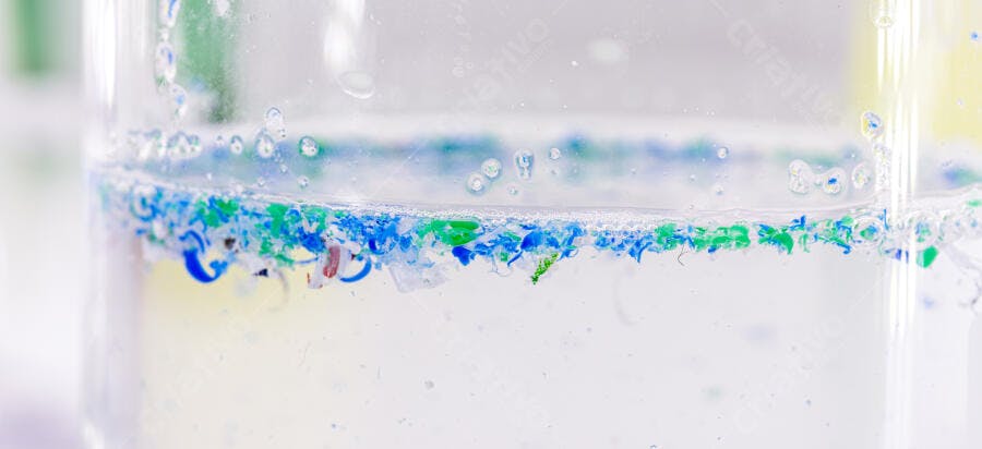Microplásticos azuis e verdes flutuando em água de laboratório