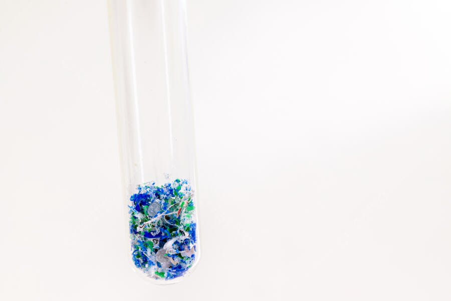 Tubo de ensaio com microplásticos azuis e verdes em estudo de poluição ambiental
