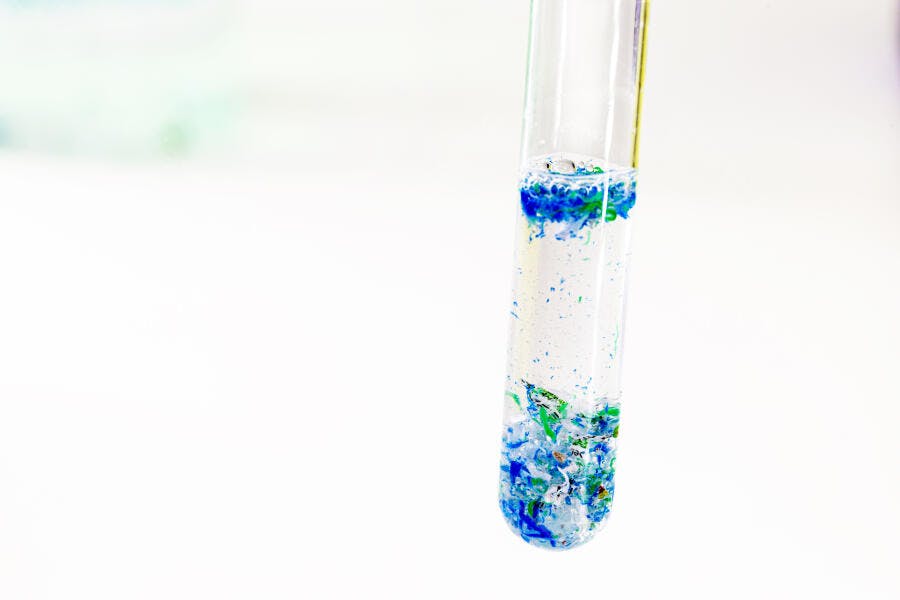 Tubo de ensaio com microplásticos azuis e verdes em estudo laboratorial