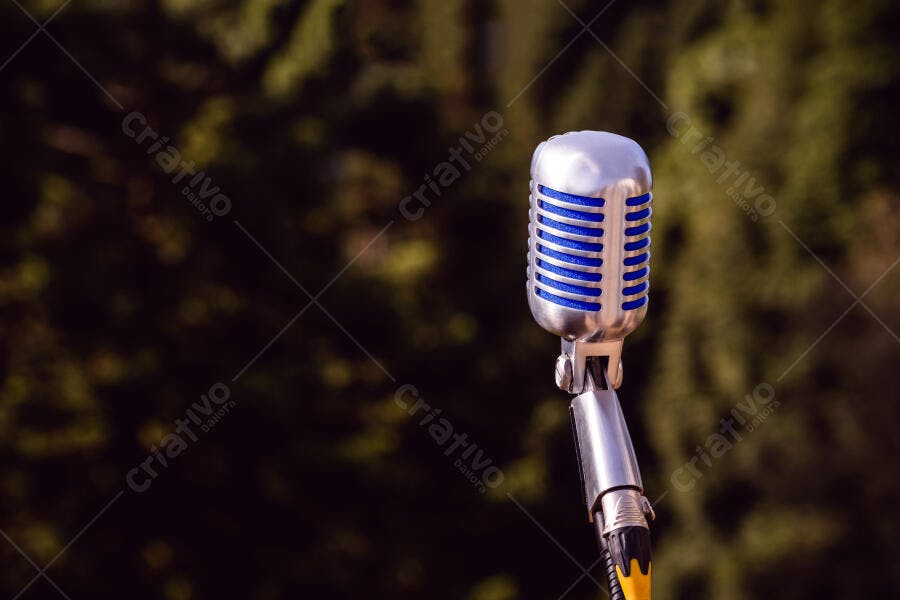 Microfone vintage prateado com grade azul em fundo desfocado verdejante