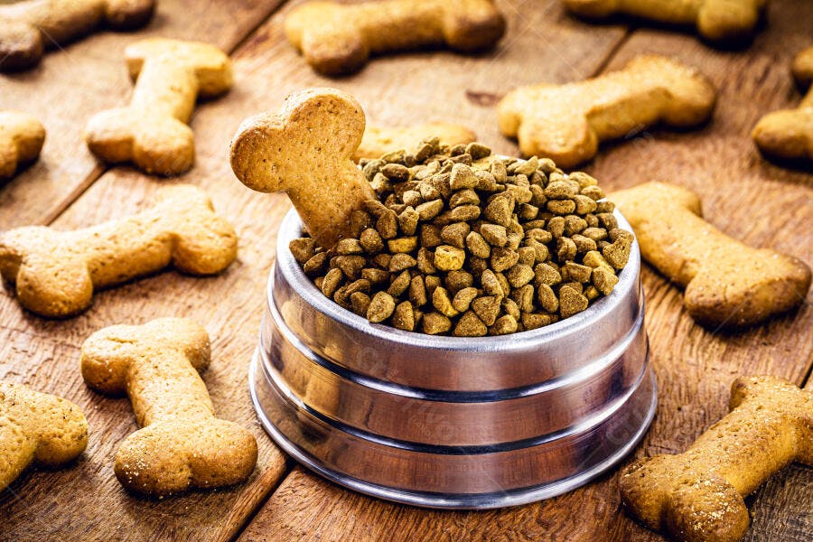 Ração e biscoitos de osso para cachorro em tigela metálica sobre madeira rústica