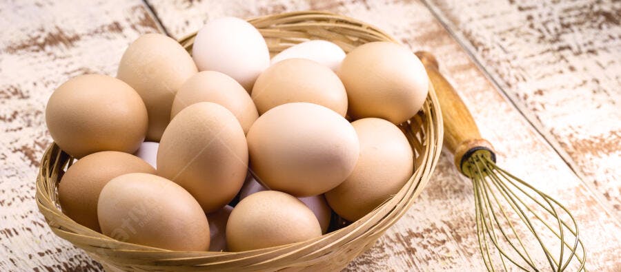 Ovos frescos brancos e marrons em cesta rústica com batedor de arame