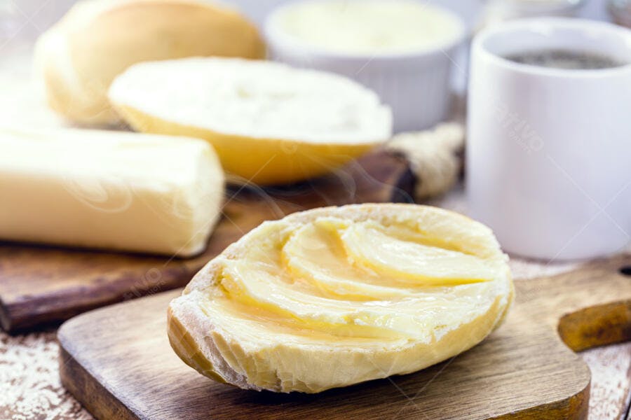 Pão francês com manteiga e café da manhã em tábua rústica