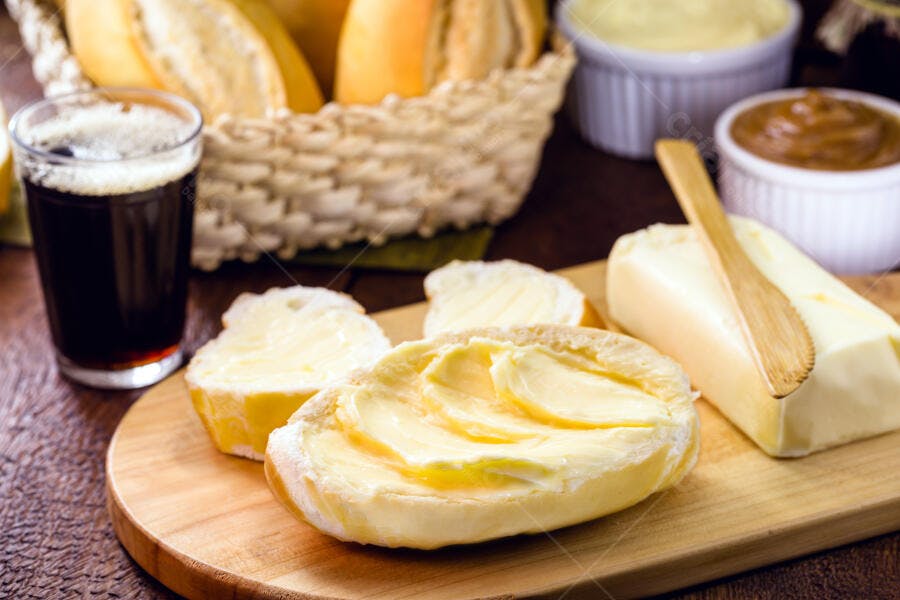 Pão francês fresco com manteiga cremosa e café na tábua de madeira