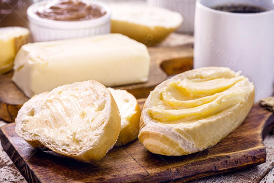 Pães franceses com manteiga e café da manhã rústico em tábua de madeira
