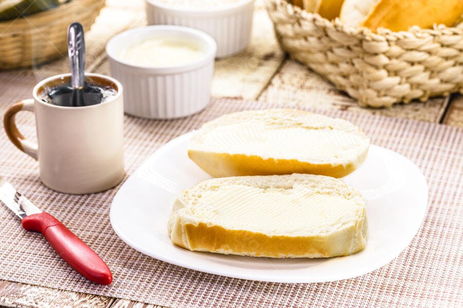 Pão francês com manteiga e café da manhã em mesa rústica