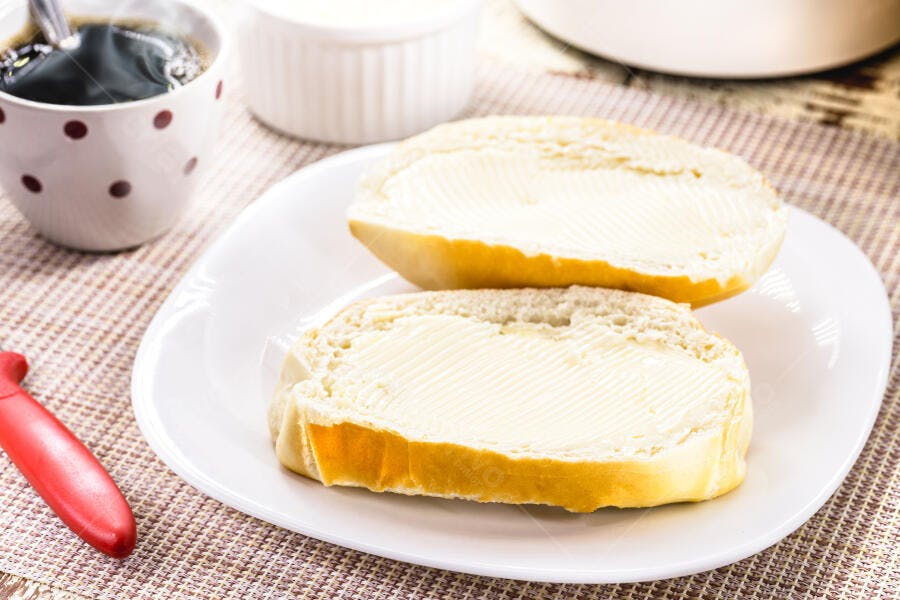 Pão francês com manteiga e café da manhã simples na mesa de casa