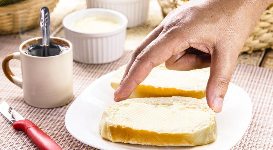 Mão de pele morena pegando pão com manteiga e café fumegante na mesa