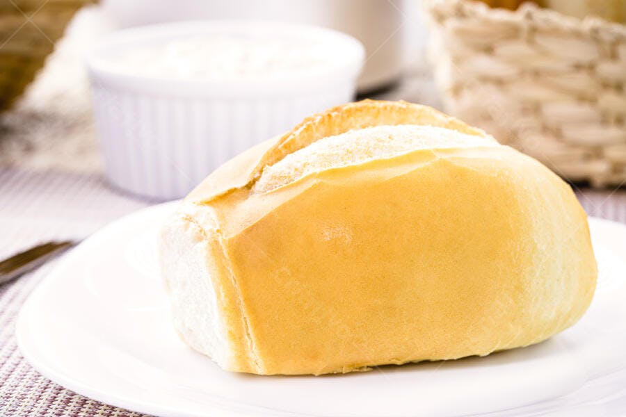 Pãozinho francês fresco em prato branco com cesta ao fundo