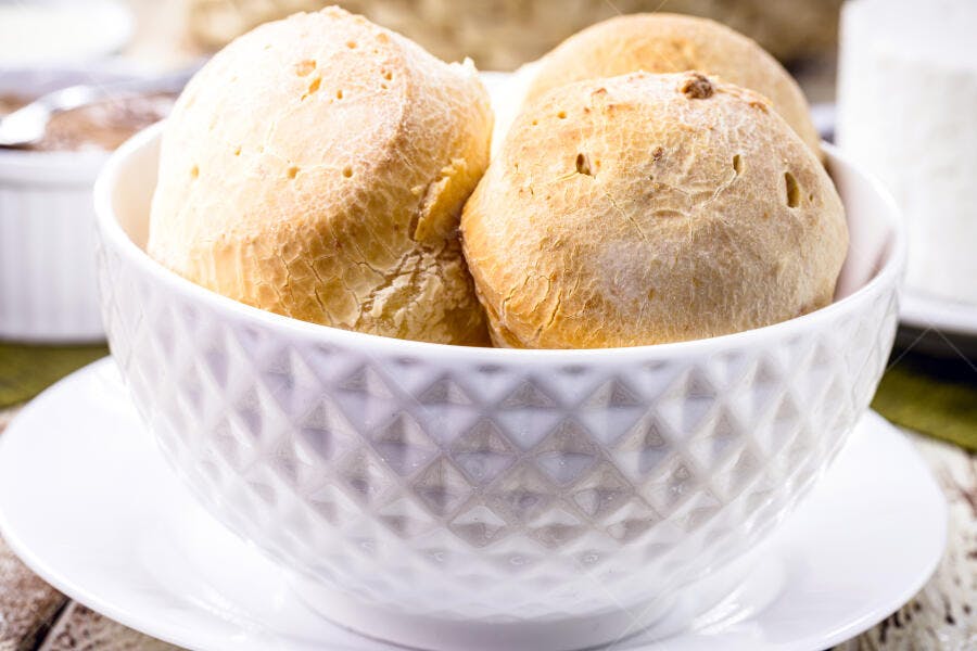 Pão de queijo fresco e dourado em tigela branca texturizada para café da manhã