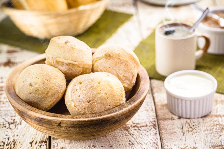 Pão de queijo quentinho em tigela de madeira com café e creme no café da manhã