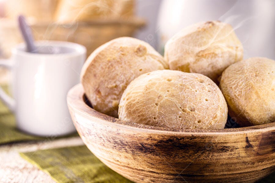 Pães de queijo dourados em tigela rústica com xícara de café fumegante