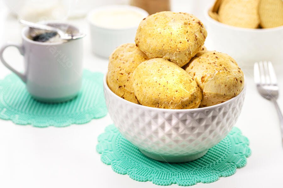 Pão de queijo dourado em tigela branca com café da manhã fresco