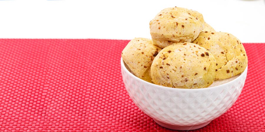 Pão de queijo quentinho em tigela branca sobre mesa vermelha