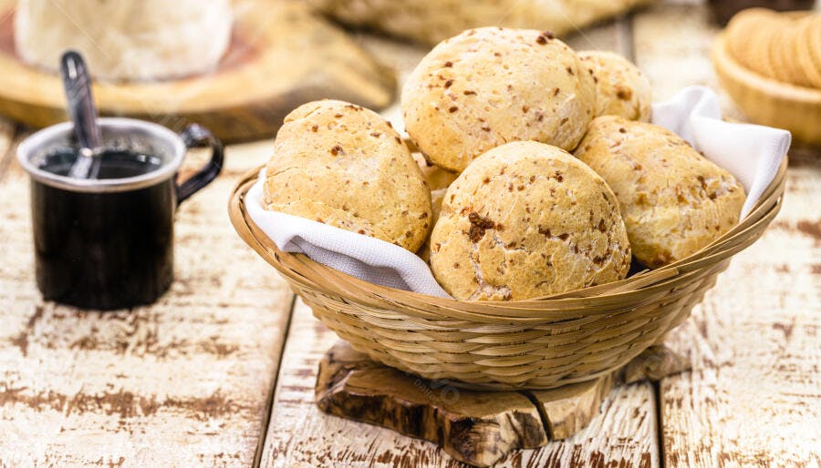 Pães de queijo frescos em cesta de vime com café preto na mesa rústica