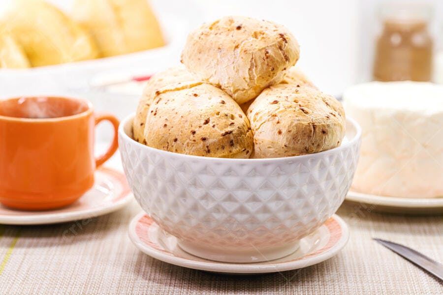 Pão de queijo em tigela branca com café na mesa do café da manhã