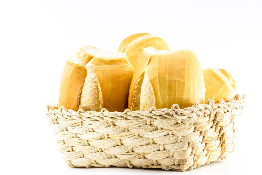 Pão francês dourado em cesto de palha sobre fundo branco